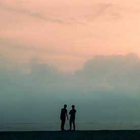 Two silhouettes beside the sea beneath a pastel sky