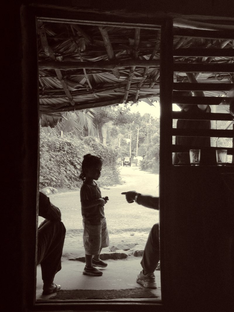 A child standing in a shaded doorway with daylight outside