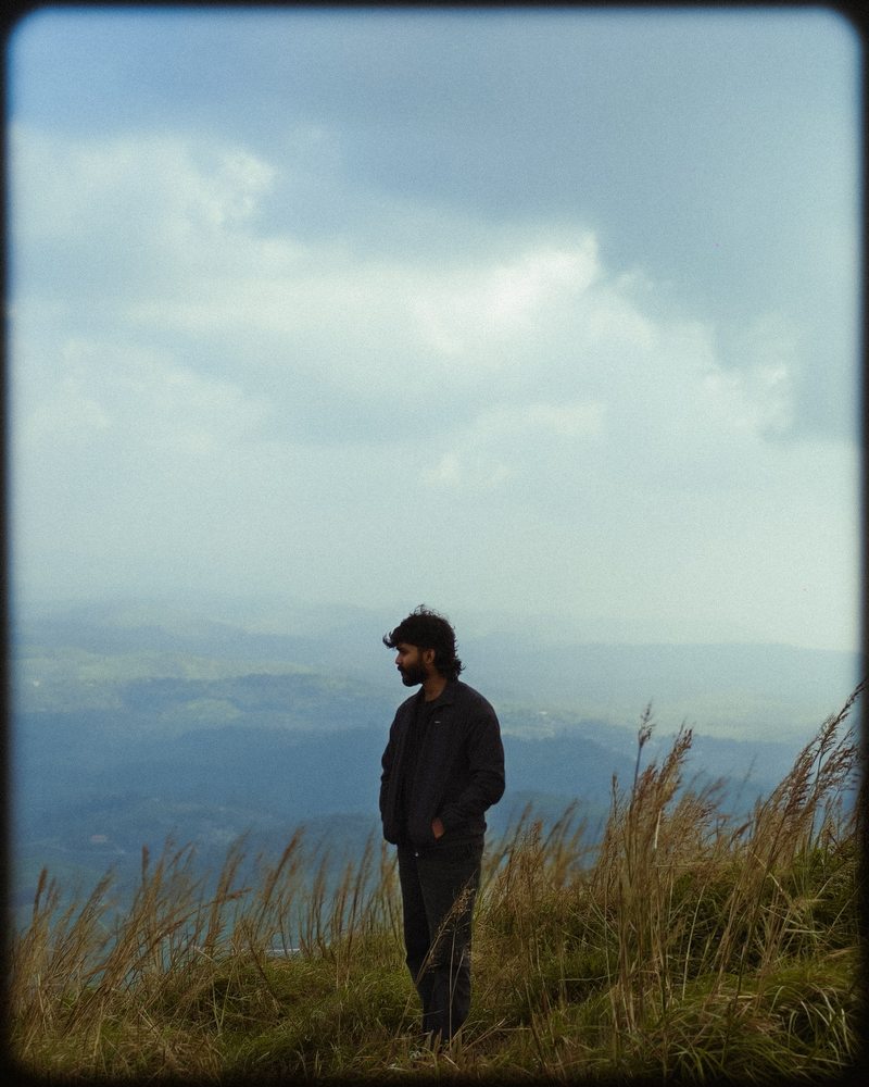 A person standing among tall grass with hazy mountain ridges behind them