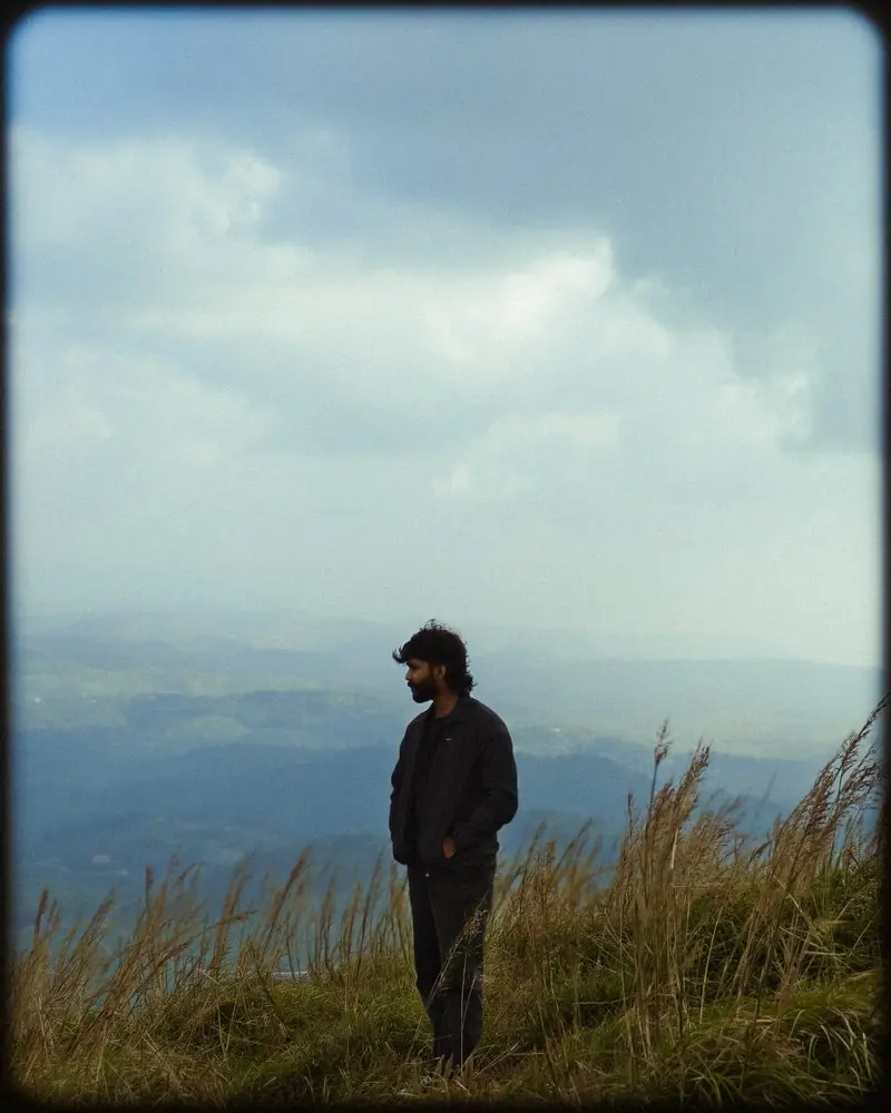 A person standing among tall grass with hazy mountain ridges behind them