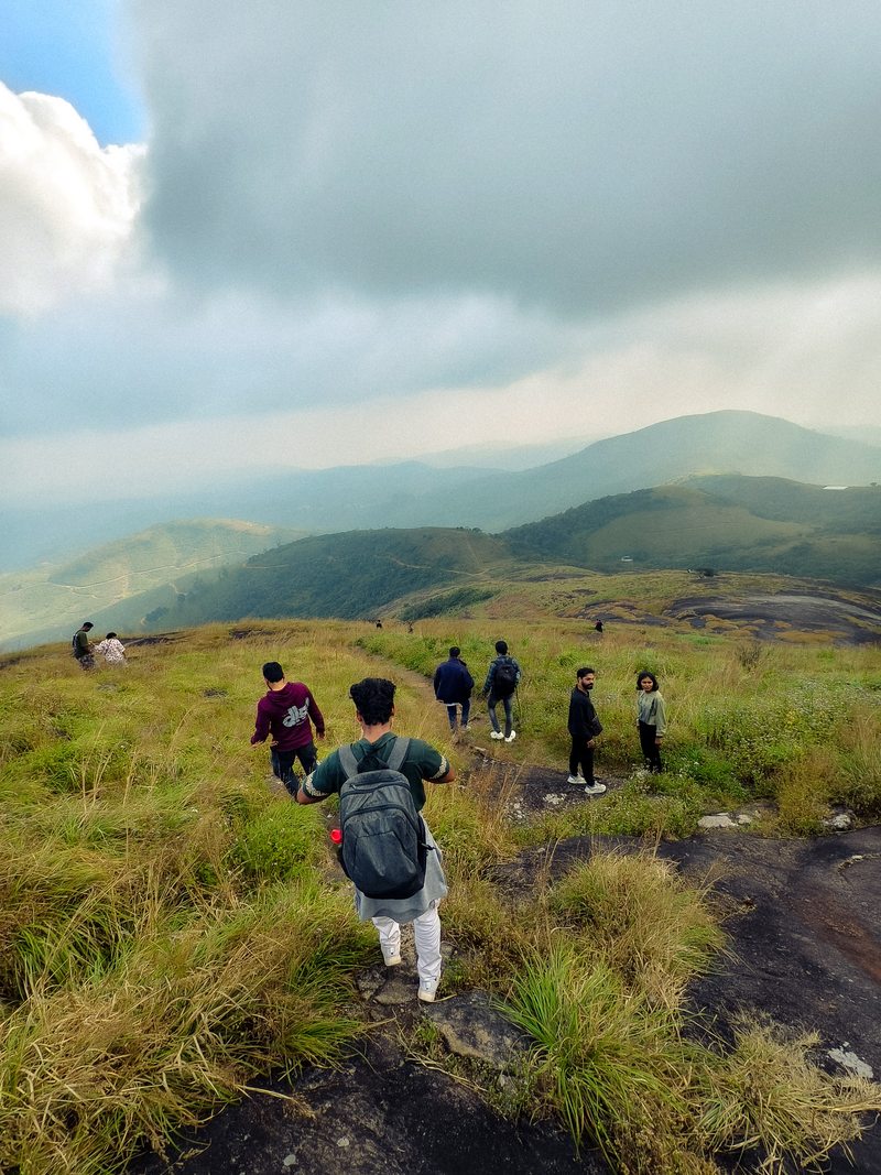 A group walking along a narrow grassy trail toward rolling green hills