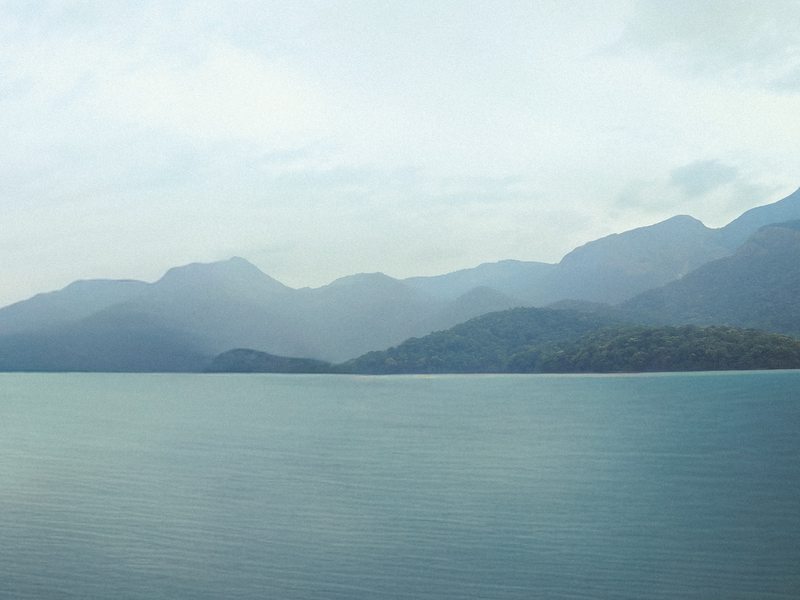 A broad lake beneath layered mountains and a pale overcast sky