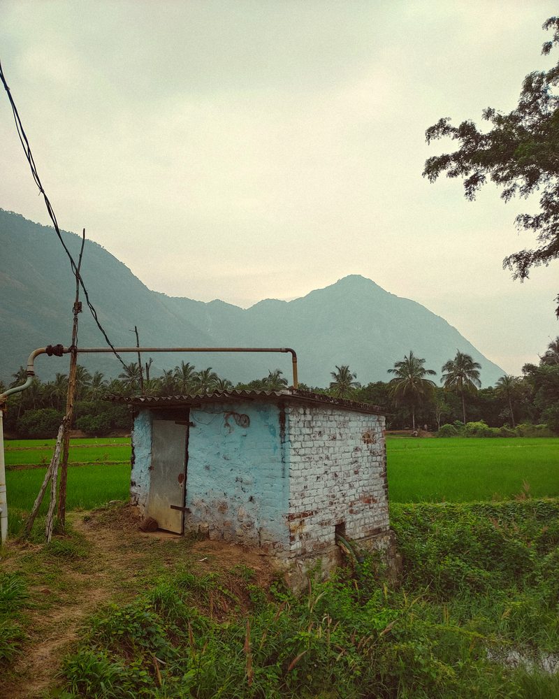 A small blue building beside green fields with mountains behind it