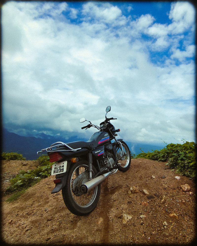 A motorcycle parked on an earth track beneath a cloud-filled mountain sky