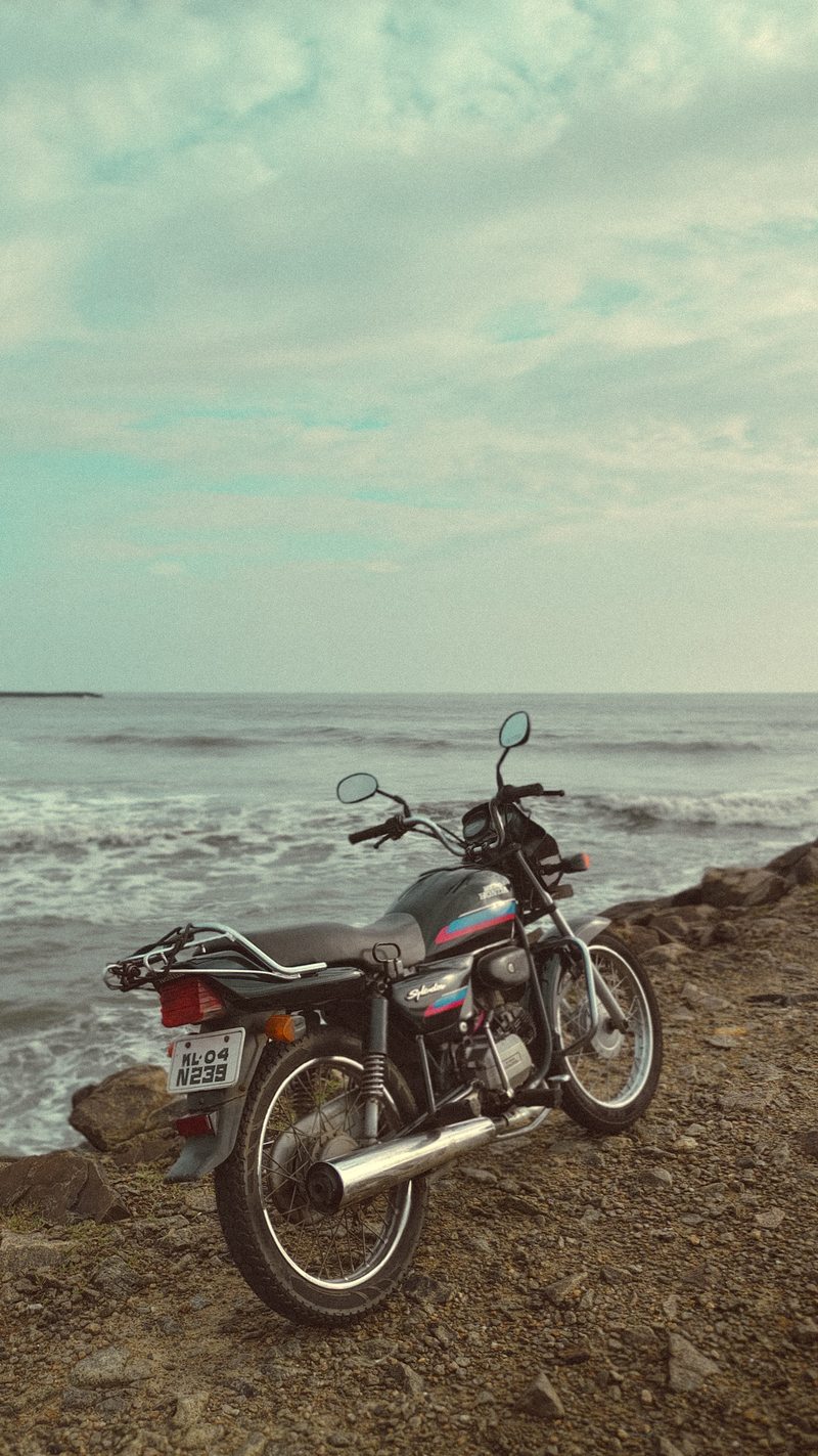 A motorcycle parked on a rocky shoreline beside the sea