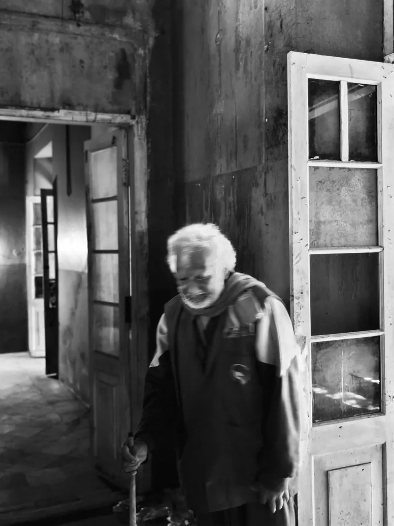An older person beside an open doorway in black and white