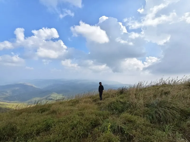A person standing on a grassy slope beneath a blue cloudy sky