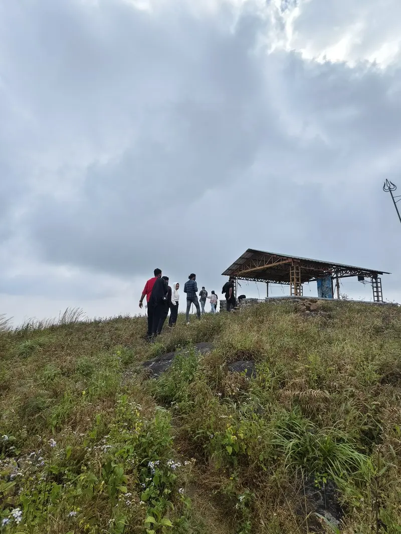 People climbing a grassy hillside toward a small shelter