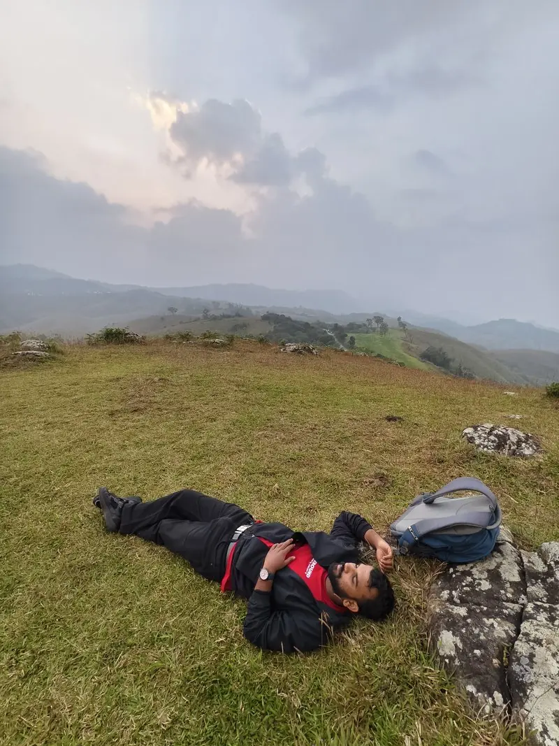 People lying back on a grassy hilltop beneath a pale evening sky