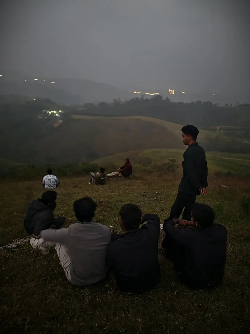 Friends sitting on a dark hillside overlooking distant lights
