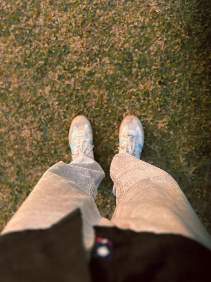 A seated persons legs and shoes above a grassy lawn