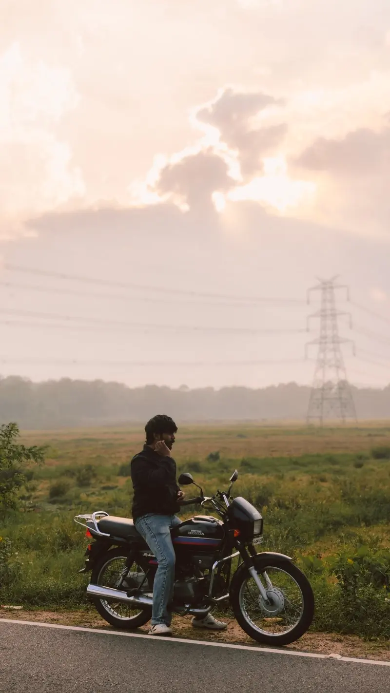 A person beside a motorcycle with fields beneath a pale sky