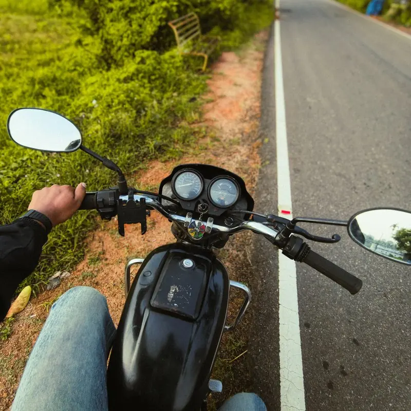 A riders view over motorcycle handlebars beside a green roadside