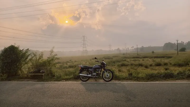 A motorcycle beside a road and fields beneath warm clouds