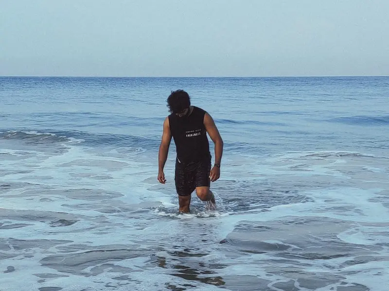 A person wading into gentle surf beneath a blue horizon