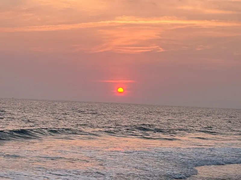 The orange sun above ocean waves beneath a pink sky